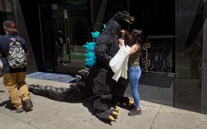 someone helping a person in a godzilla costume drink some water