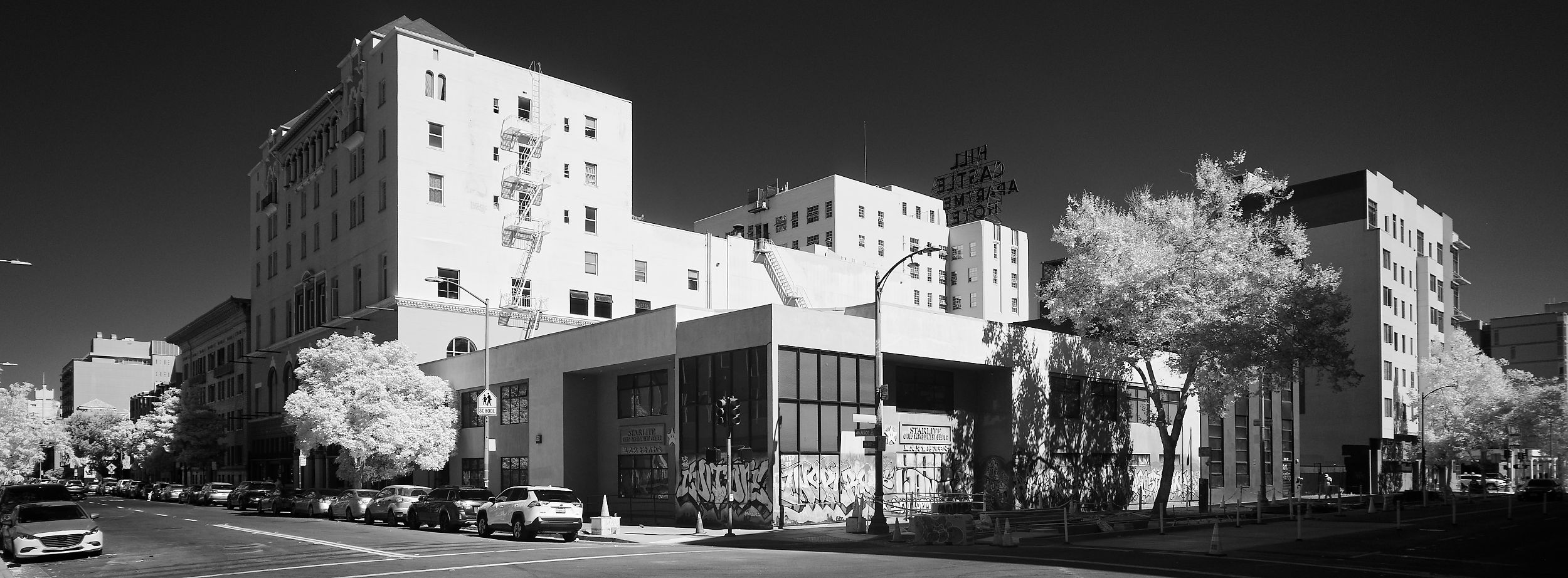 Black and white infrared wide angle photo of a city block in Oakland featuring the boarded and graffiti'd Startlite Child Development Center